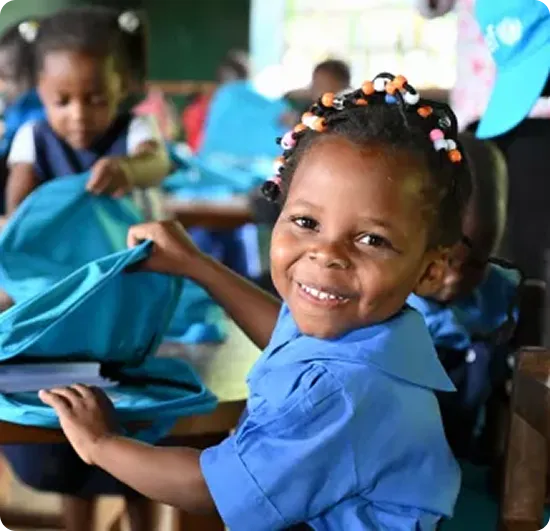 en smilende lille pige der sidder på skolebænken med en unicef taske